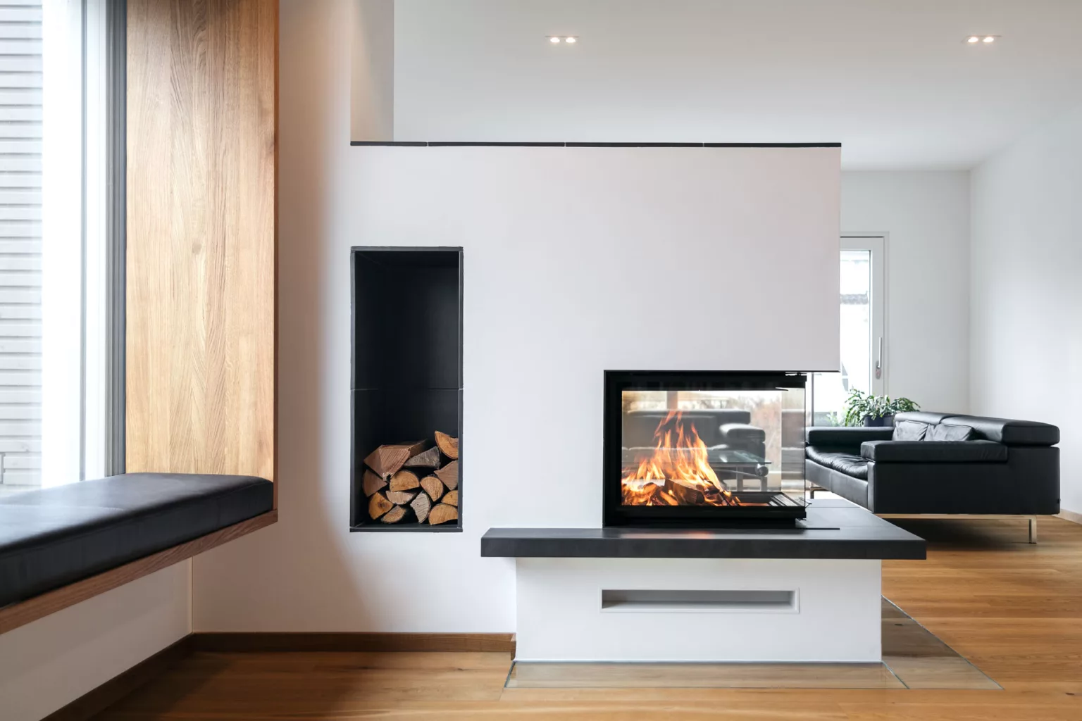 Witte ingebouwde haard met hoekglas en een nis met brandhout in een woonkamer